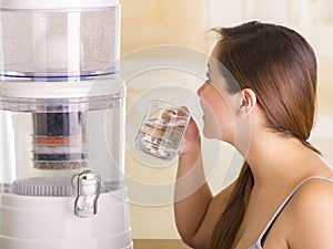 Close up of a beautiful woman drinking a glass of water with a filter system of water purifier on a kitchen background
