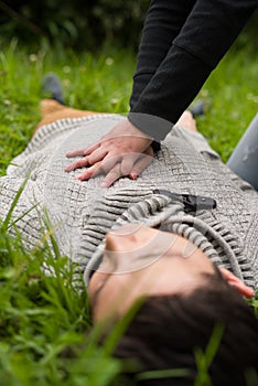 Close up of a beautiful woman giving first aid to a handsome young man, cardiopulmonary resuscitation, in a grass