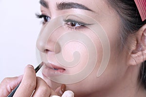 Close up beautiful woman with hands beautician or makeup artist applying lipstick on her face in studio