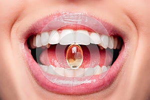 Close Up Of Beautiful Woman Opened Mouth Holding Fish Oil Pill In White Teeth. Smiling Girl Holding Capsule With Omega-3 Between