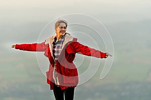 Close up beautiful woman stand near cliff with background of grass field and rural village area in view on the mountain with warm