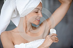 Close up beautiful woman wearing towel applying antiperspirant after shower