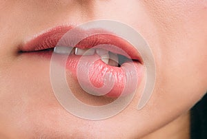 Close up of beautiful women`s lips covered with lipstick. Bite lower lip. White teeth. Sexy move. Cut view.