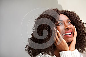 Close up beautiful young african woman with curly hair looking away with hands on face