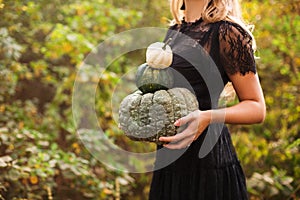 Close up of beautiful young blond woman with long straight hair, wearing black guipure dress, holding pumpkins