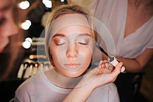 Close up beautiful young blonde woman face. She has eyeshadows on eyeline. Make up artist use mascara. Hairdresser work photo