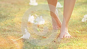 Close up beautiful young female feet barefoot walking on green grass with white flowers background. Morning outdoors exercise in a photo