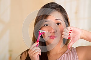 Close up of a beautiful young funny woman with an shaver on her face with a thumps down, in bath background