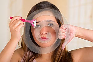 Close up of a beautiful young funny woman with an shaver on her face with a thumps down, in bath background