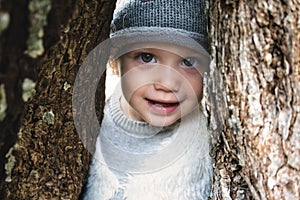 Close up of beautiful young girl model smiling and peering through a gap between tree trunks in the woods wearing winter clothes