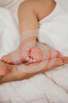 Close-up. Beautiful young mother holds in her hands the legs of the baby. Beautiful young mother plays with the baby in bed.