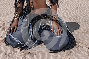 Close up of beautiful young stylish tribal dancer in oriental costume sitting on sand outdoors