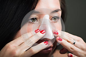 Close up of a beautiful young woman aplying a white nose mask to clean the skin photo