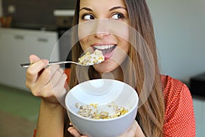 Close up of beautiful young woman eating skyr yogurt with cereal muesli fruit at home, looking to the side, focus on the model