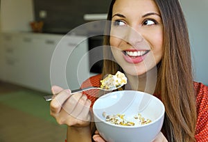 Close up of beautiful young woman eating skyr yogurt with cereal muesli fruit at home, looking to the side, focus on the model