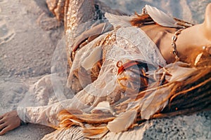 Close up of beautiful young woman in elegant dress lying on sand on the beach at sunset time