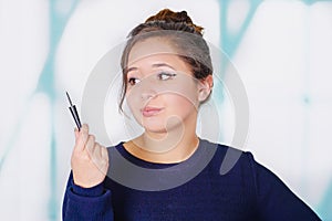 Close up of beautiful young woman holding a eyeliner in her hand, in a blurred background