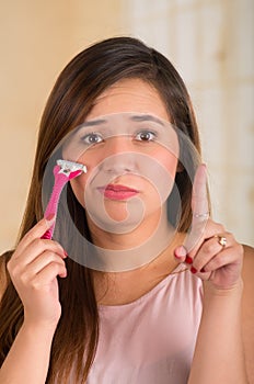 Close up of a beautiful young woman holding a shaver with onde hand and pointing to the sky with her other hand, in a