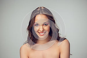 Close up of beautiful young woman with long healthy curly hair and bright make up isolated on grey studio backgroud