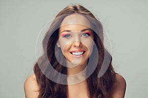 Close up of beautiful young woman with long healthy curly hair and bright make up isolated on grey studio backgroud