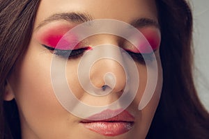 Close up of beautiful young woman with long healthy curly hair and bright make up isolated on grey studio backgroud