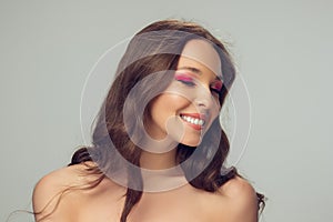 Close up of beautiful young woman with long healthy curly hair and bright make up isolated on grey studio backgroud, shy