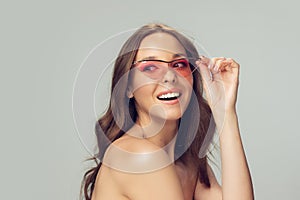 Close up of beautiful young woman with long healthy curly hair and bright make up wearing stylish pink eyewear isolated