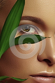 Close-up beautiful young woman with smooth tanned skin with green leaves. Beauty model with natural bronze make-up