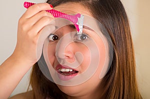 Close up of a beautiful young woman using a shaver on her eyebrow