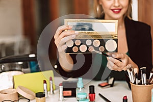 Close up beauty blogger holding eye shadow palette and make up brush in hands while talking about cosmetic products