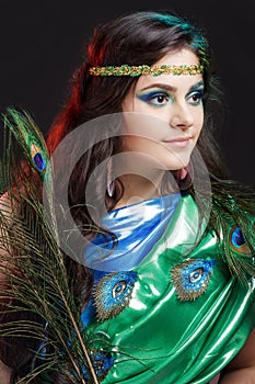 Close up beauty portrait of beautiful girl with peacock feather, headband. Creative makeup peafowl feathers. Attractive