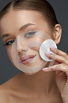 Close up beauty portrait of cute young attractive woman cleaning her face with a cotton pad.