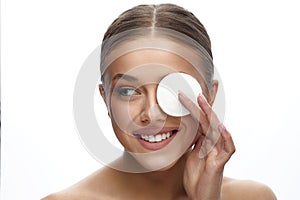 Close up beauty portrait of a young attractive woman cleaning her face with a cotton pad isolated over white background.