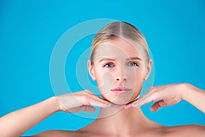 Close up Beauty portrait of young woman blonde touching her face on blue background. Perfect Fresh Skin. Youth and Skin