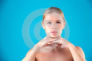 Close up Beauty portrait of young woman blonde touching her face on blue background. Perfect Fresh Skin. Youth and Skin