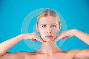 Close up Beauty portrait of young woman blonde touching her face on blue background. Perfect Fresh Skin. Youth and Skin