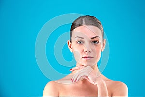 Close up Beauty portrait of young woman brunette smiling and touching her face on blue background. Perfect Fresh Skin