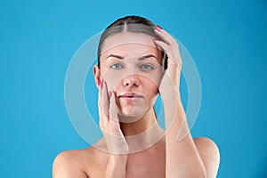 Close up Beauty portrait of young woman brunette smiling and touching her face on blue background. Perfect Fresh Skin