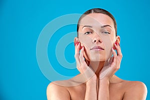 Close up Beauty portrait of young woman brunette smiling and touching her face on blue background. Perfect Fresh Skin