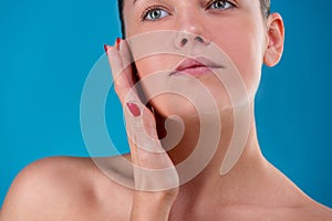 Close up Beauty portrait of young woman brunette smiling and touching her face on blue background. Perfect Fresh Skin