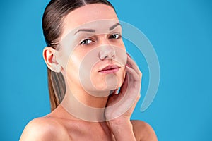 Close up Beauty portrait of young woman brunette smiling and touching her face on blue background. Perfect Fresh Skin