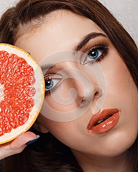 Close-up beauty portrait of young woman with grapefruit with beautiful nude makeup. Modern smokey eyes with colorful eyeshadows