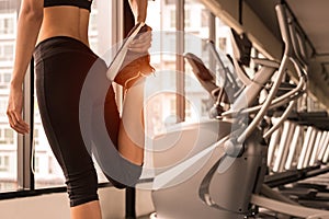 Close up beauty woman stretching legs in workout fitness gym center with sport equipment and treadmill background. Sporty girl wa