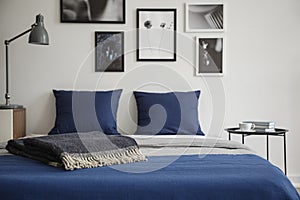 Close-up of bed with blue bedding and dark colored blanket. Bedside table with books and coffee next to it.