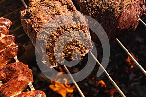 Close up of beef and sausage roasting on a spit with ember and fire