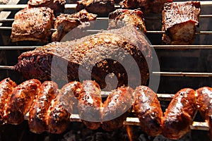 Close up of beef and sausage roasting on a spit with ember and fire