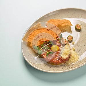 Close up of beef tartar with capers and small toasts. Served on a gray textured plate over pastel blue mint background.