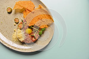 Close up of beef tartar with capers and small toasts. Served on a gray textured plate over pastel blue mint background.