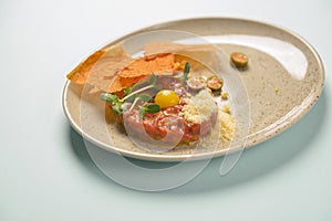 Close up of beef tartar with capers and small toasts. Served on a gray textured plate over pastel blue mint background.