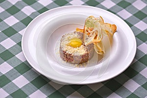 Close up of beef tartar with capers and small toasts. Served on a white plate over green plaid tablecloth background.